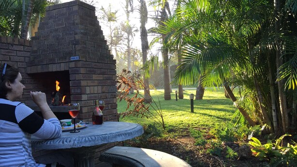 A woman sitting at a stone table with a brick oven in the background, surrounded by lush greenery. - Low Tide (St. Lucia)
