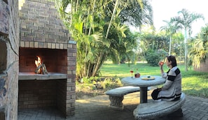 A brick fireplace with a fire, surrounded by lush greenery and a stone bench.