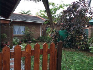 A brick house with a tiled roof, a wooden fence, and a garden with various plants and a green water tank.
