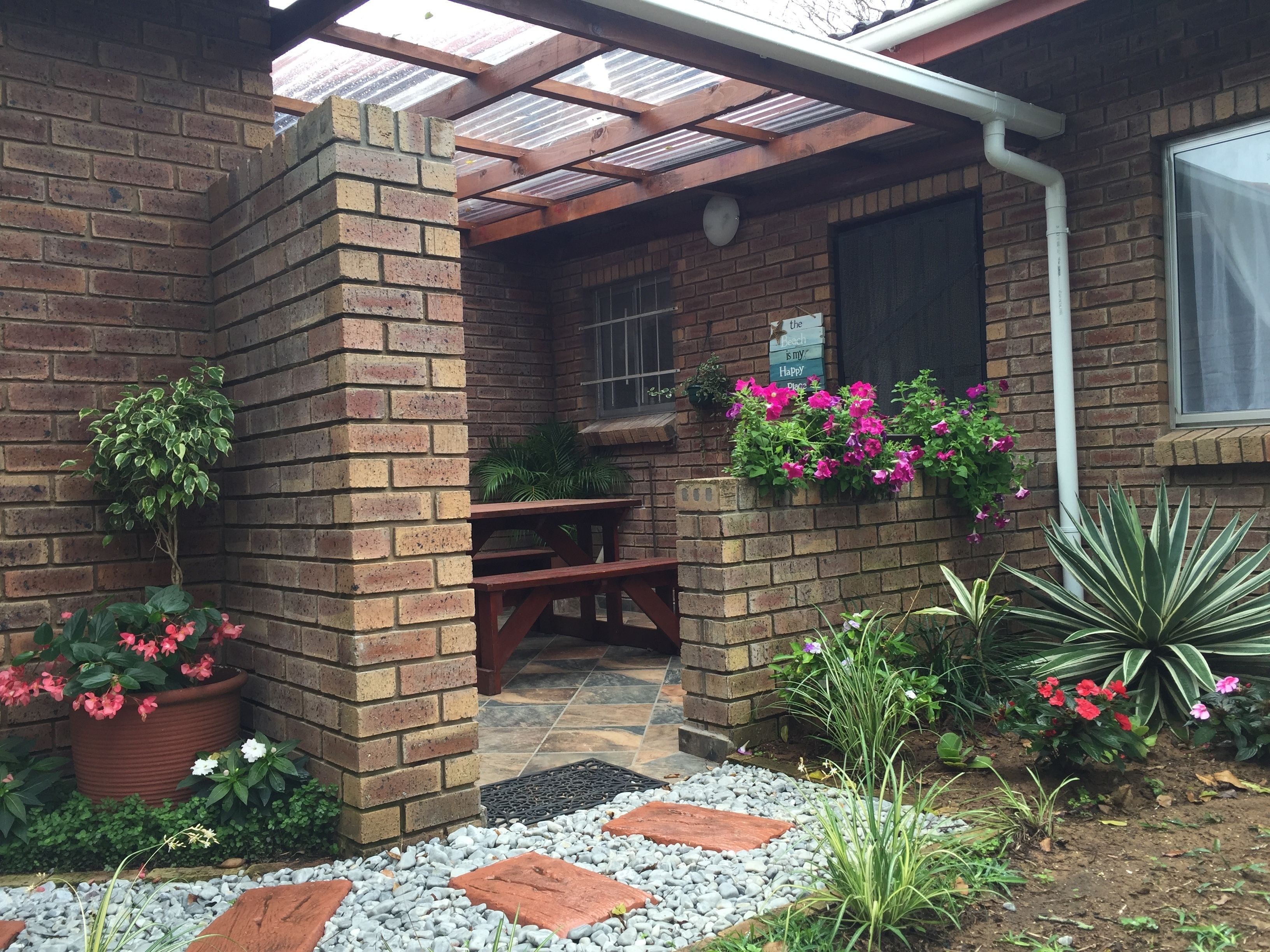 A brick patio with a wooden table and benches, surrounded by potted plants and flowers.