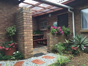 A brick patio with a wooden table and benches, surrounded by potted plants and flowers.