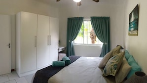 A bedroom with a bed, a wardrobe, a window with curtains, and a painting on the wall. - Low Tide (St. Lucia)