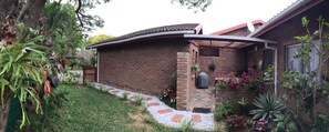A brick house with a tiled roof, a garden with stepping stones, and a variety of plants and flowers.