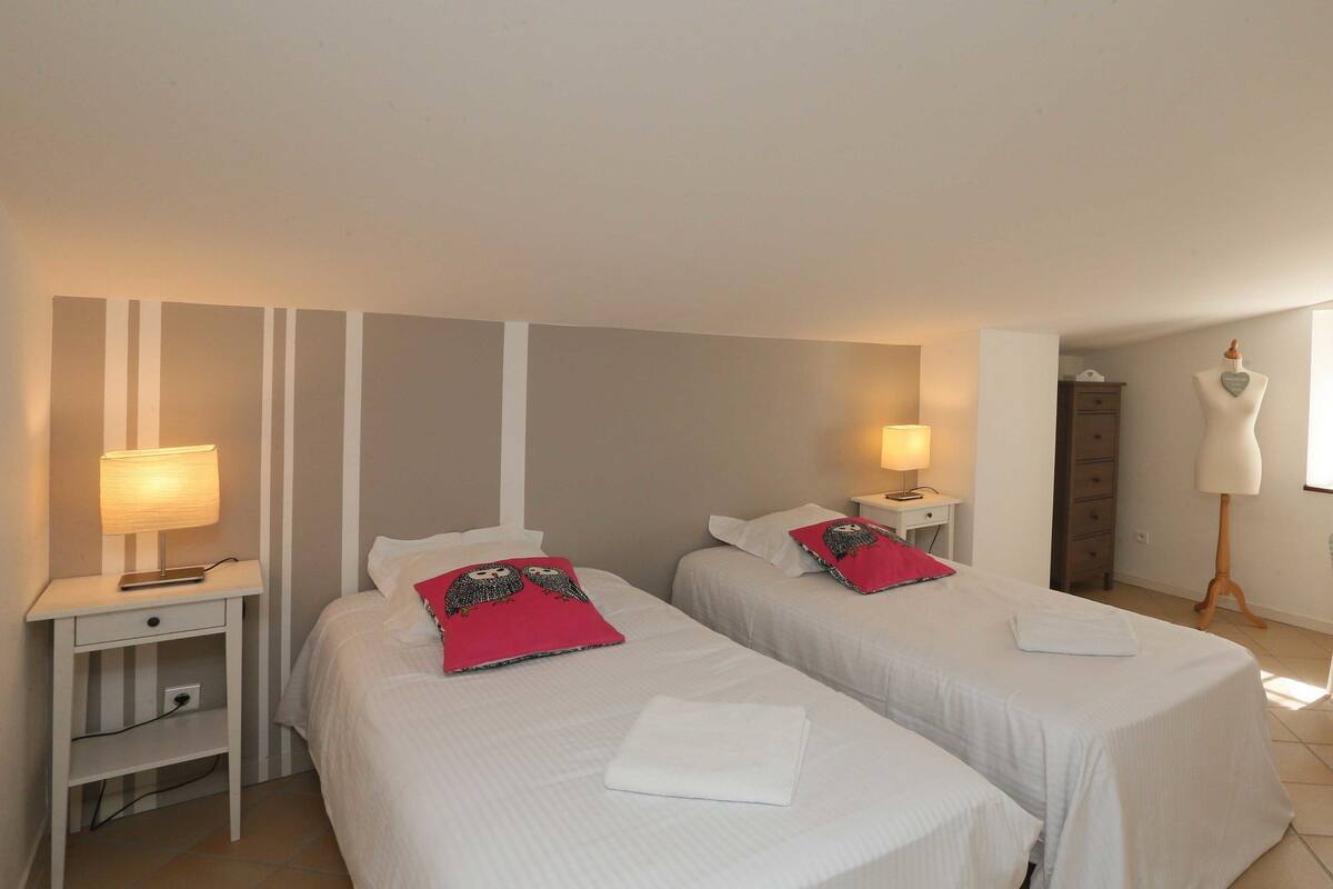 Habitació d'hotel amb dos llits, nits, una arca de vestir, una cadira i un maniquí.