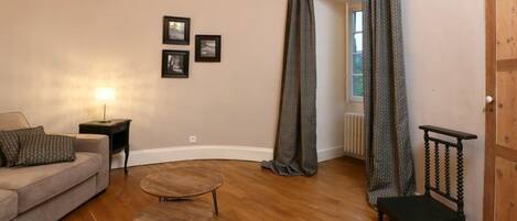 A living room with a sofa, two small tables, a chair, a lamp, and a door with a curtain.