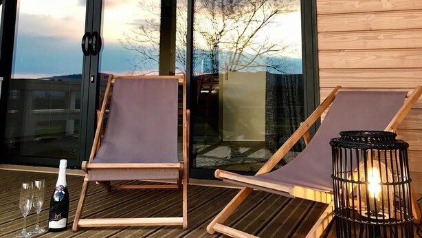Een houten terras met twee loungesteilen, een tafel met een fles en glazen, en een kandelaar.