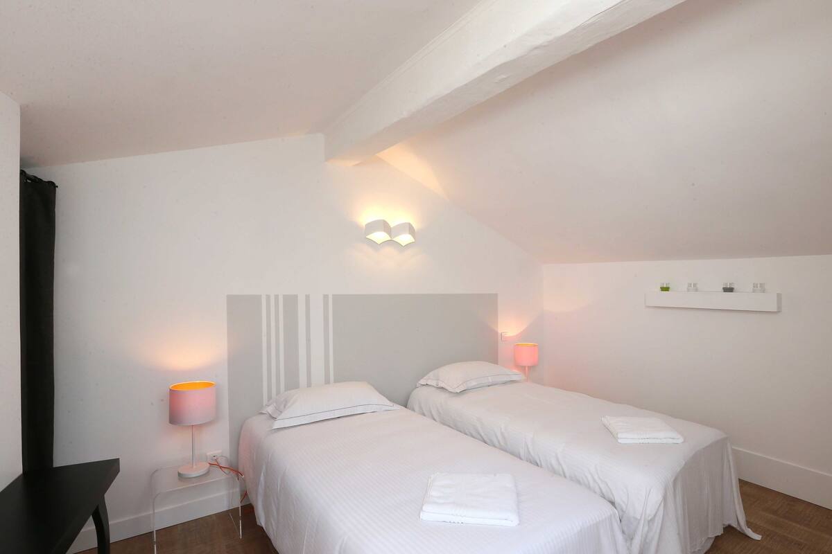 Habitació d'hotel amb dos llits, una tauleta de nit, una làmpada i un lluminari fixat a la paret.