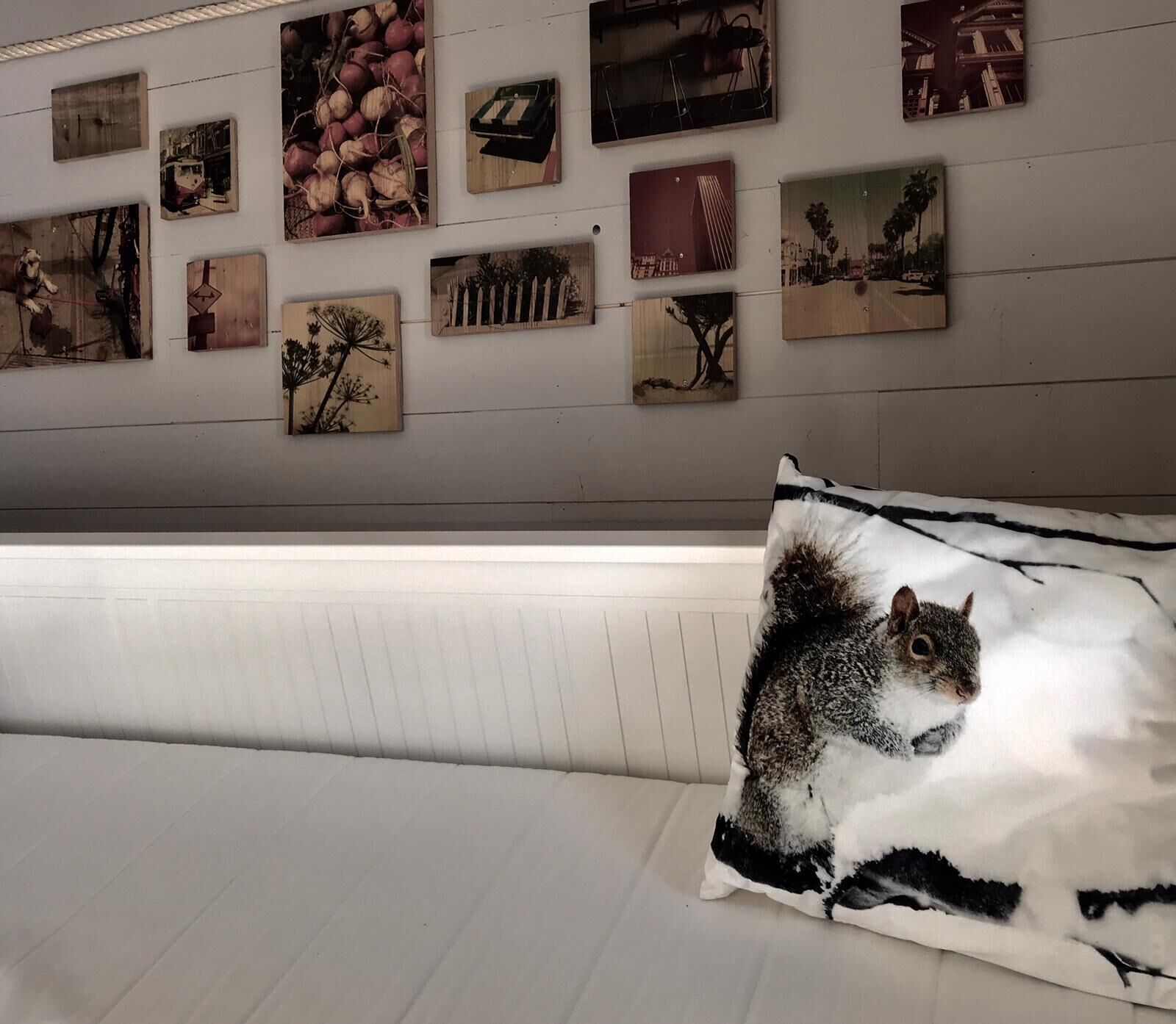Une pièce avec un banc recouvert d’un tissu blanc et un mur orné de divers tableaux encadrés.
