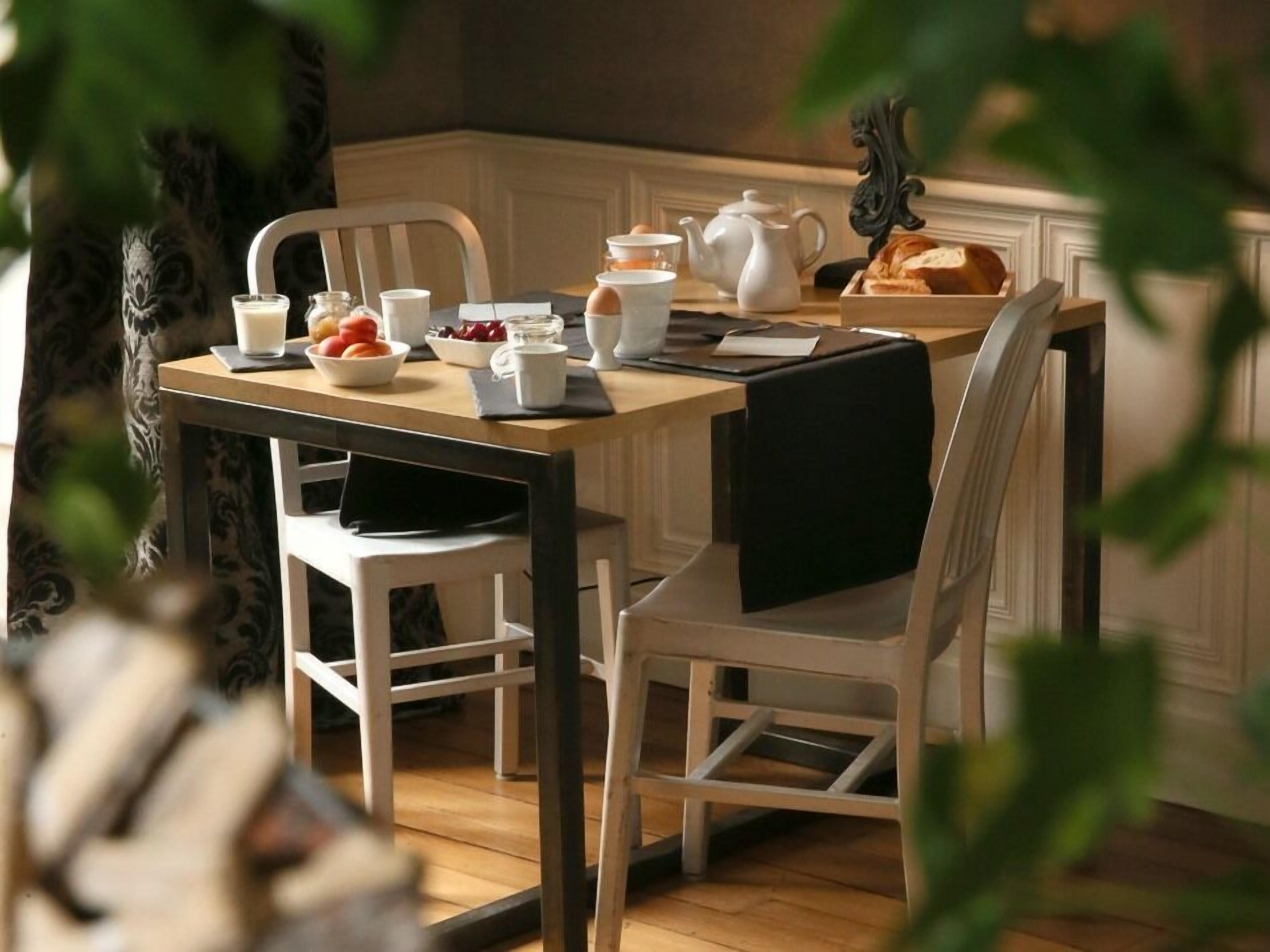 A dining table with chairs, a teapot, cups, and a fruit bowl.
