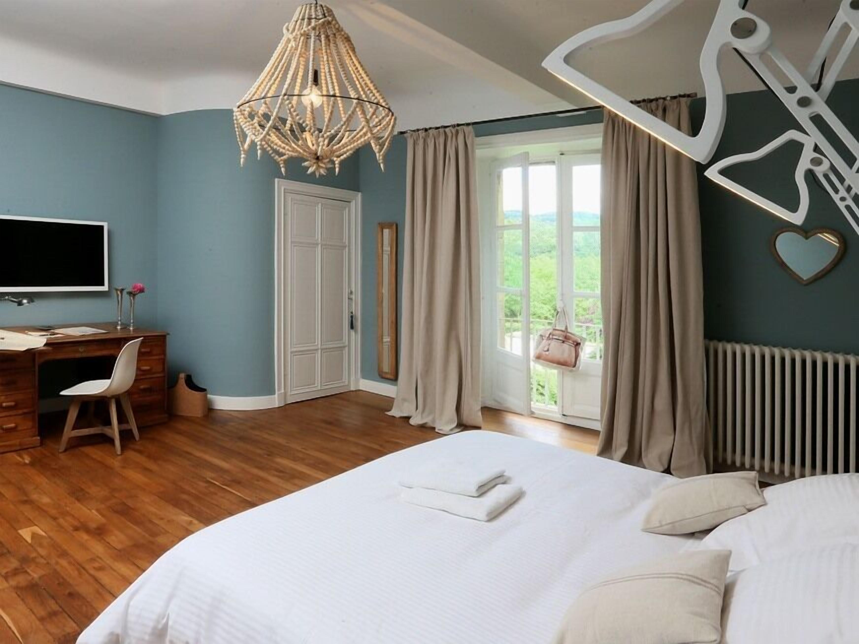 A bedroom with a bed, a desk, a chair, a television, and a window with curtains.