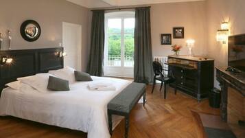 Ein Hotelzimmer mit einem großen Bett, einem Schreibtisch, einem Sessel und Blick auf Grünflächen durch das Fenster.