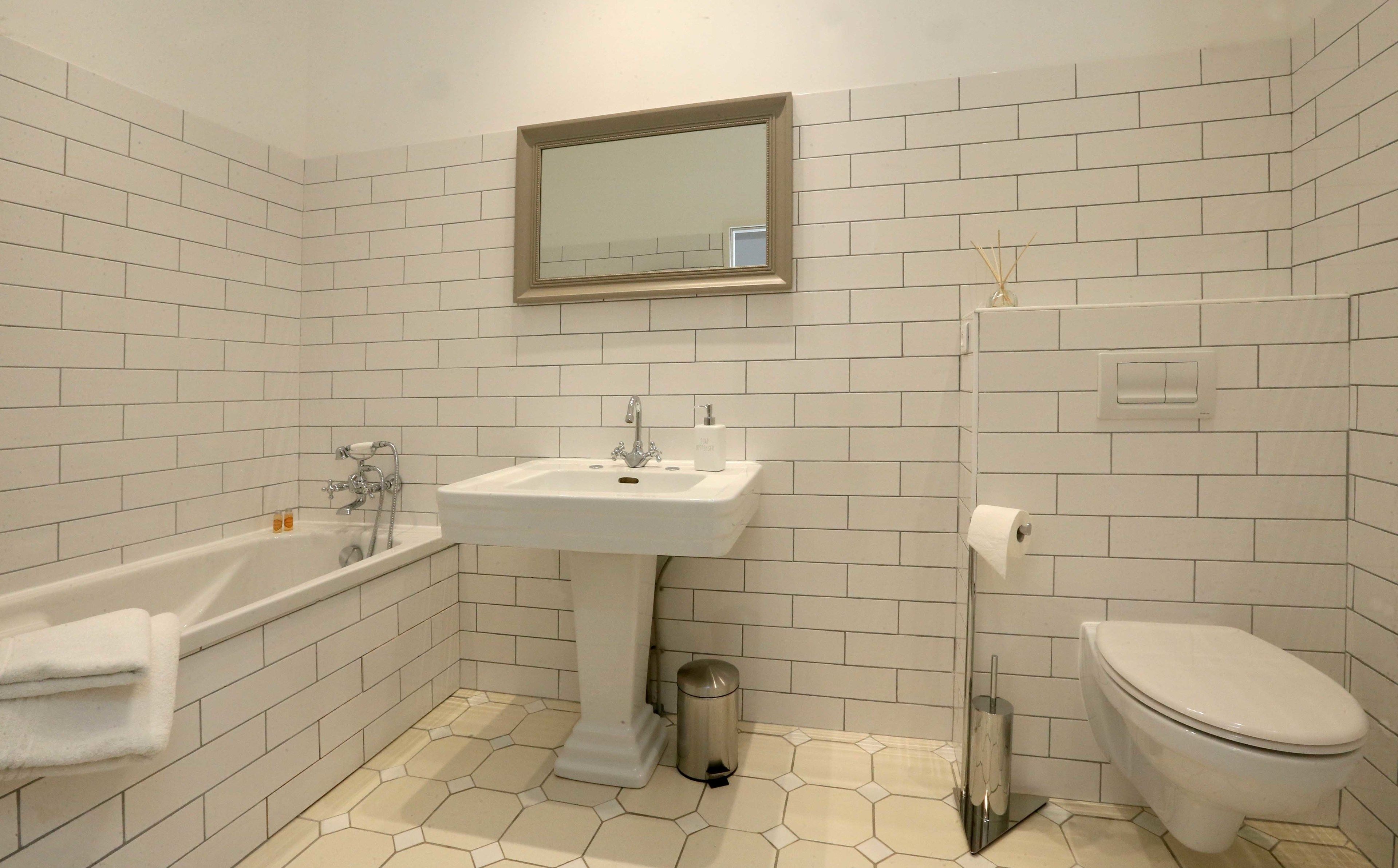 A bathroom with white tiled walls, a white sink, a bathtub, and a toilet.