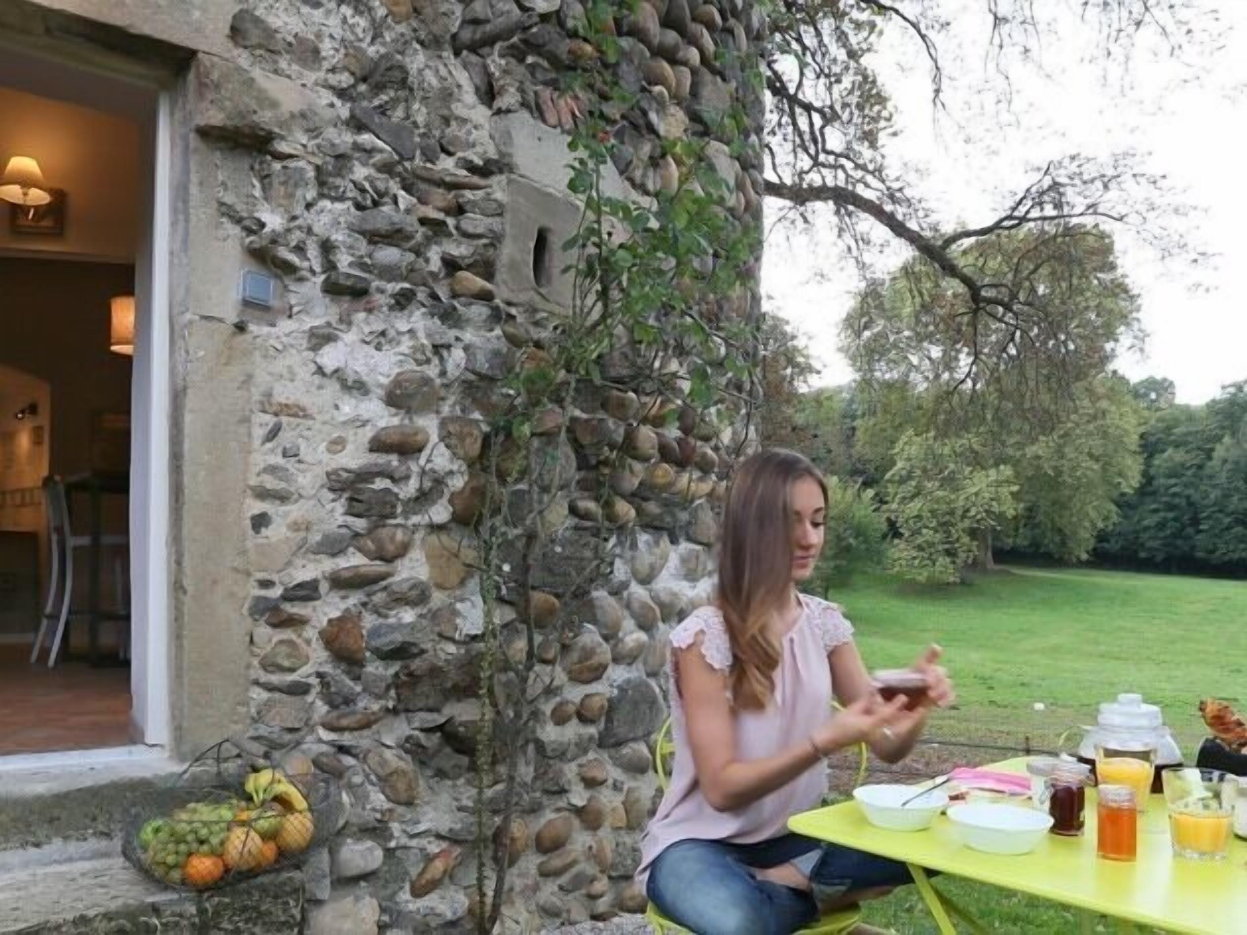 A person sitting at an outdoor table with a meal, surrounded by a stone wall and greenery.