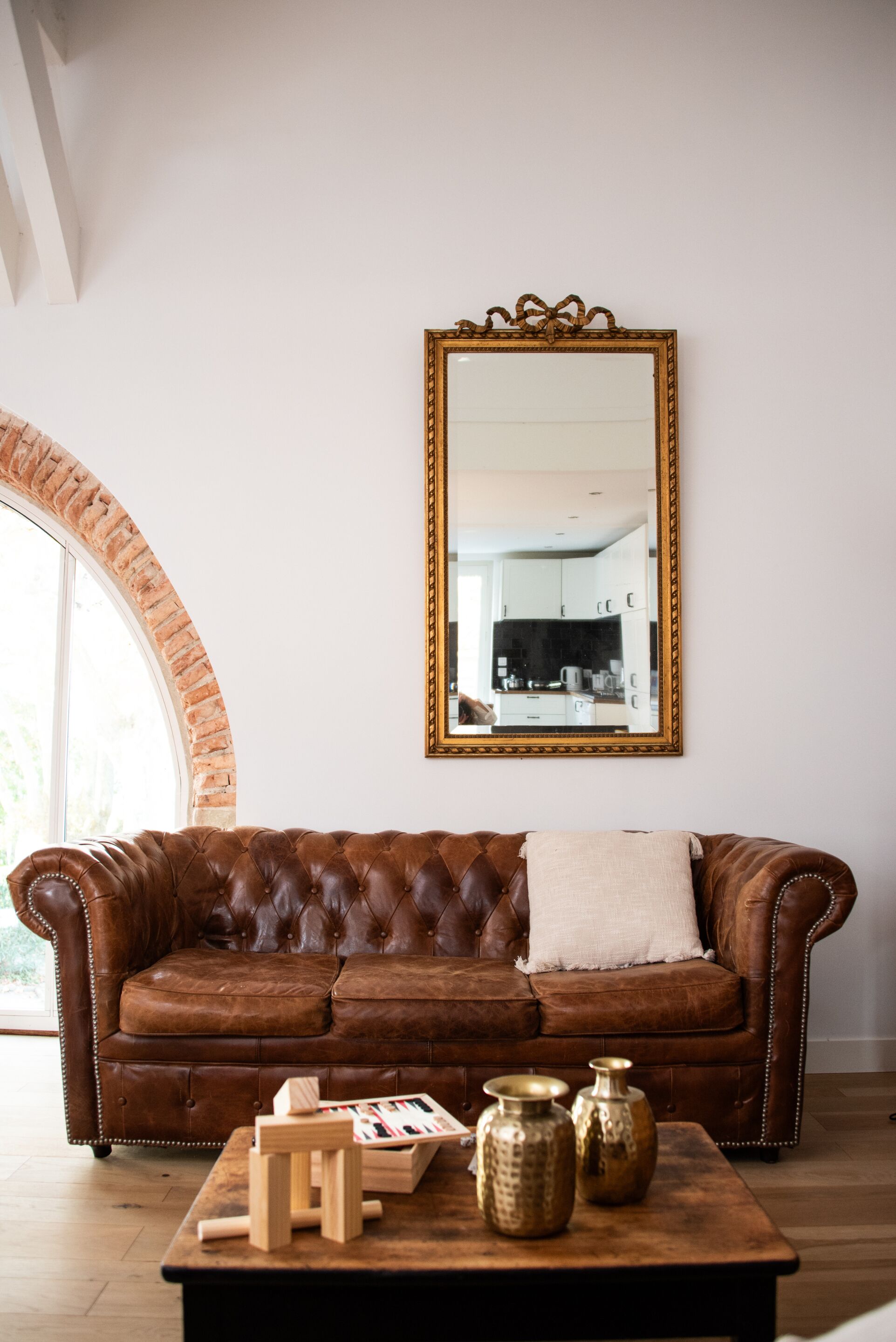Un canapé en cuir marron avec un coussin blanc, une table basse en bois ornée de vases décoratifs et un grand miroir au mur.