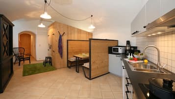 Una cocina compacta con microondas, cafetera y lavabo. Hay una zona de comedor con una mesa y sillas, y una partición de madera.