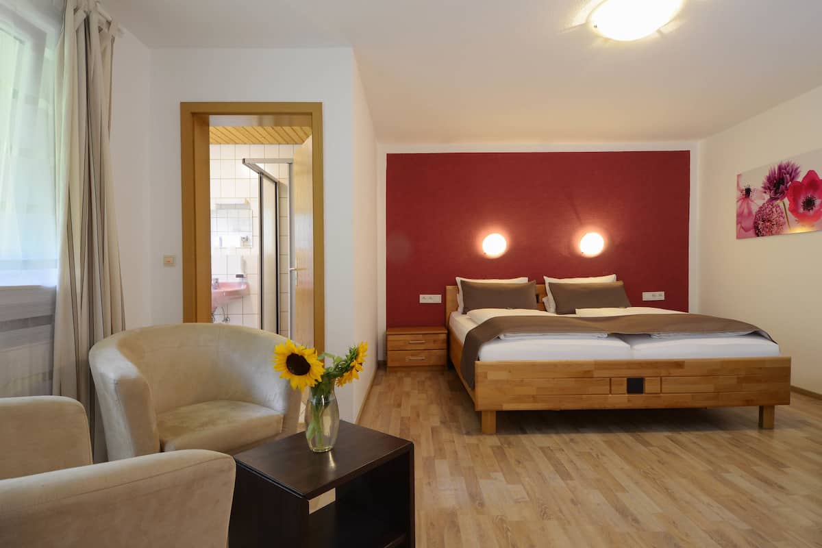 Ein Schlafzimmer mit einem hölzernen Bett, einem Sessel, einem Nachttisch und einer Vase mit Blumen.