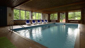 Une piscine intérieure dotée d’un plafond en bois, de grandes fenêtres et de chaises longues bleues.