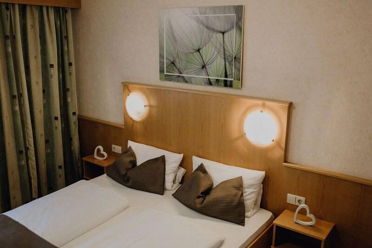 Ein Hotelzimmer mit einem hölzernen Kopfteil, zwei Nachttischlampen, einem Bett mit weißer und brauner Bettwäsche und einem Wandbild von Löwenzahn.