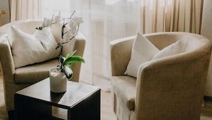 Un salon avec deux fauteuils beiges, une table basse noire et un vase contenant des fleurs blanches.