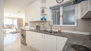 Eine moderne Küche mit weißen Schränken, einer eingebauten Waschmaschine, einem großen Fenster und einer Uhr an der Wand.