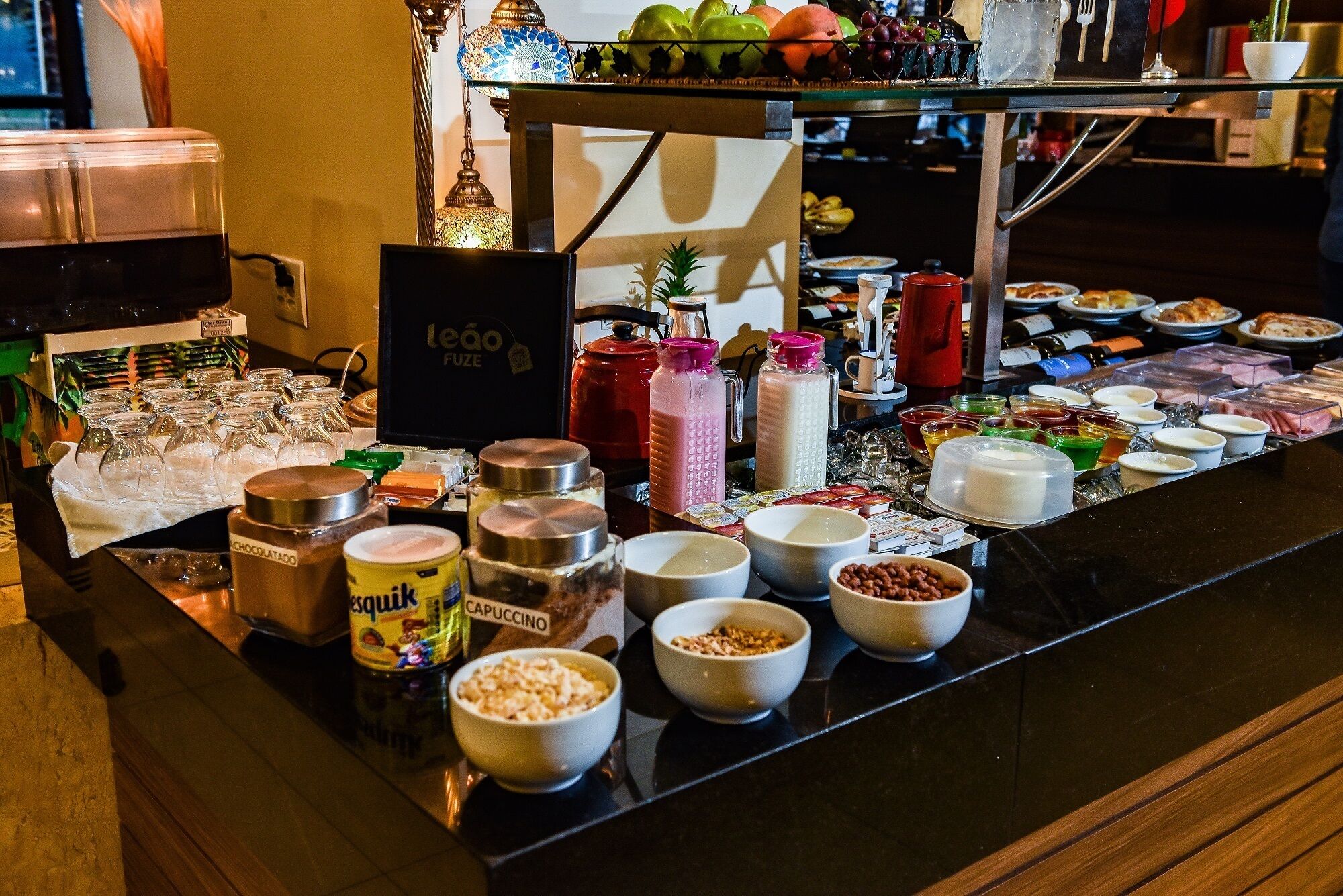 A buffet with various food items and beverages, including jars of chocolate and cappuccino, and a coffee machine.