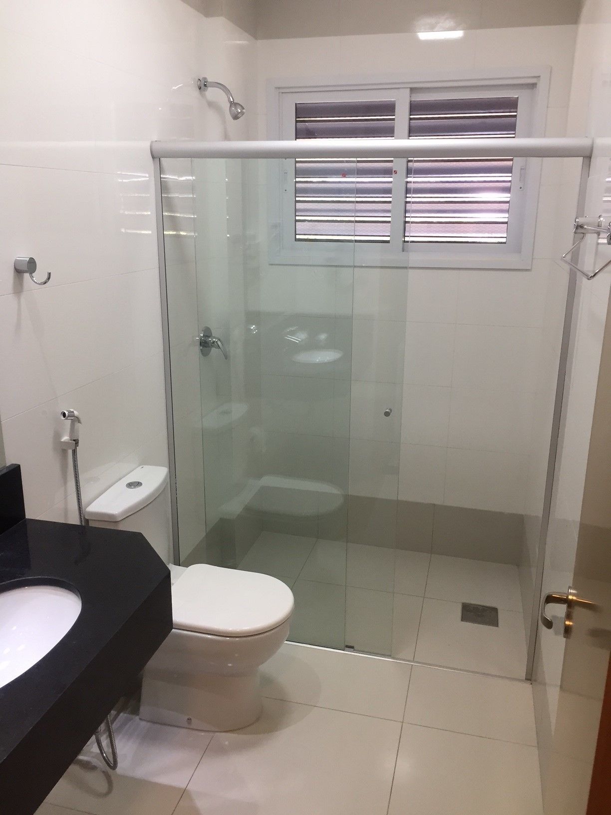 Un baño moderno con cabina de ducha de vidrio, inodoro blanco y lavamanos negro.