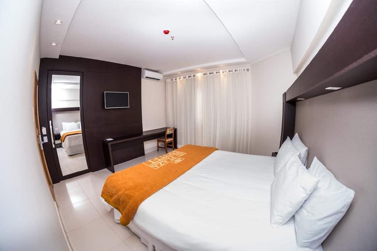Habitación de hotel con cama, escritorio, silla, televisor y baño visible a través de una puerta abierta.