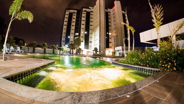 Een hotel met een zwembad, palmbomen en een modern gebouw op de achtergrond.