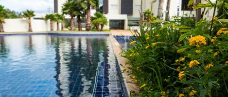 A swimming pool with tiled edges, surrounded by greenery and yellow flowers.