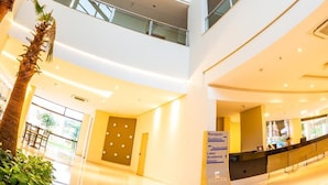 Een meerlaags atrium met een centrale trap, palmbomen en een receptiebalie.