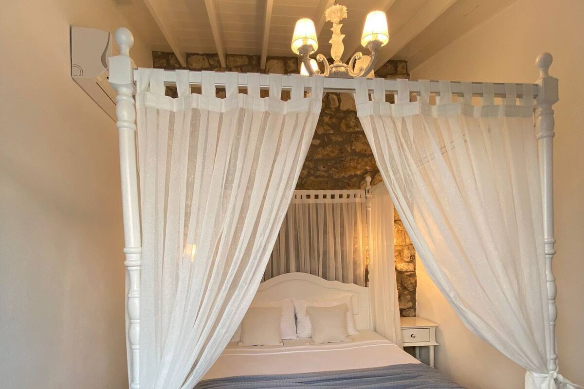 A four-poster canopy bed with a stone wall backdrop, a nightstand, and a chandelier.