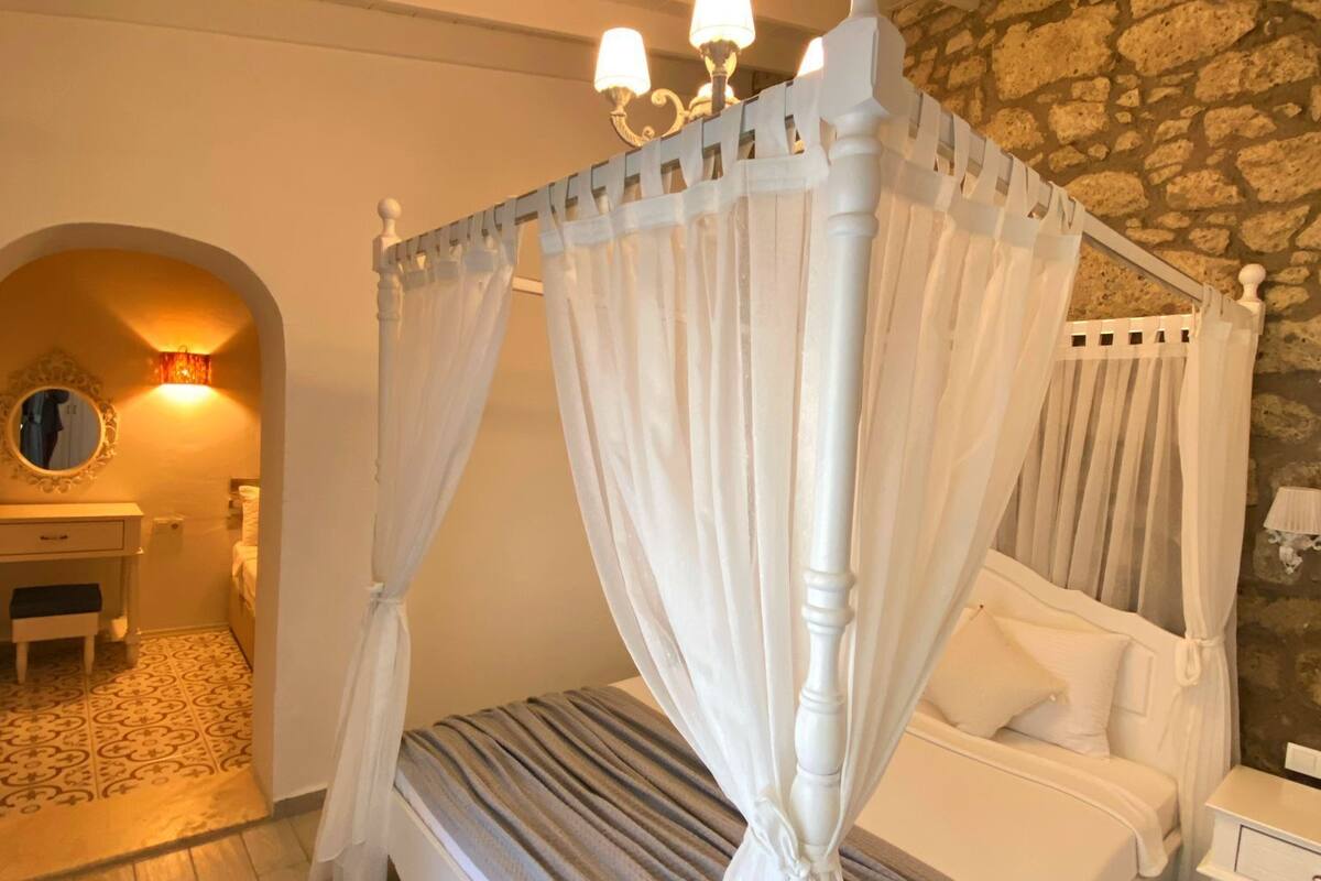 A bedroom with a four-poster bed, a stone wall, and a small desk with a mirror.