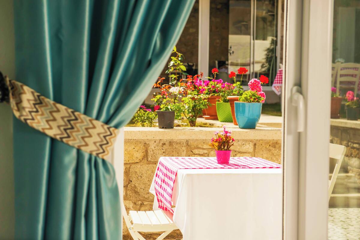 A patio with a table covered in a checkered tablecloth, surrounded by potted plants and flowers.