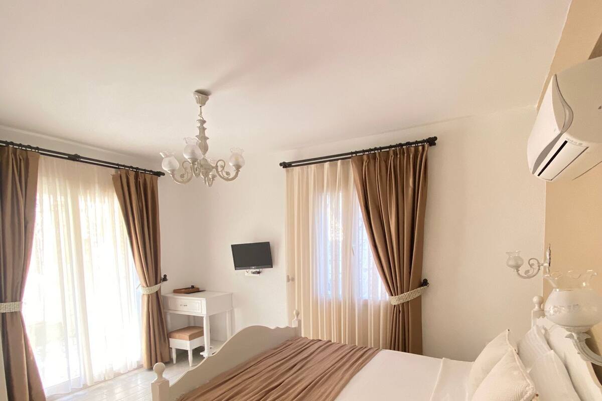 A bedroom with a bed, bedside table, TV, and a desk with a chair.