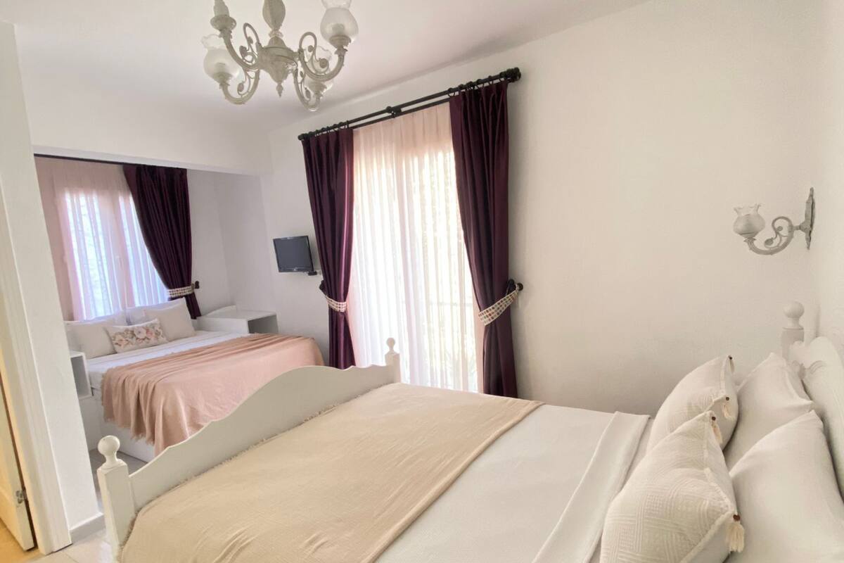 A bedroom with a large bed, a chandelier, and a view of another room with a sofa.