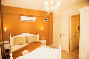 A bedroom with a bed, bedside tables, an air conditioning unit, a chandelier, and a door. - Selin Hotel (Cesme)