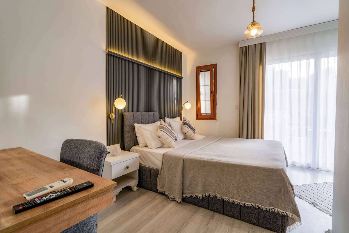Quarto de hotel com cama, mesa de cabeceira, luminária e vista para o exterior.