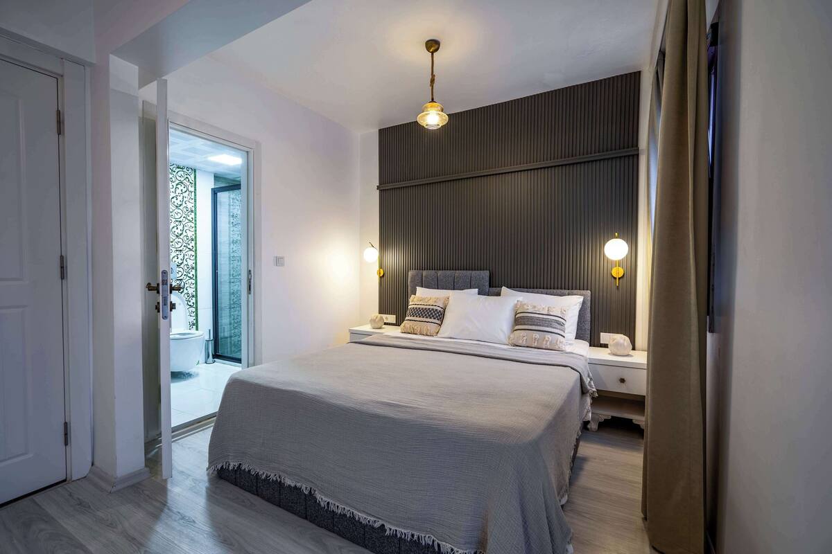 Quarto com cama grande, luminárias de cabeceira e vista para uma varanda.