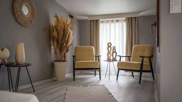 Una sala de estar moderna con una paleta de colores neutros, que incluye dos sillones, una mesa de centro, un espejo grande y una planta en maceta.