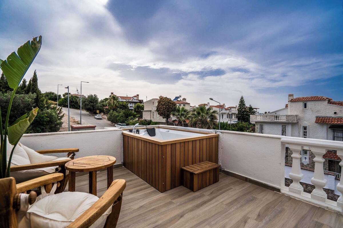 Terraço no telhado com banheira de hidromassagem, mobiliário de madeira e vista para a cidade.