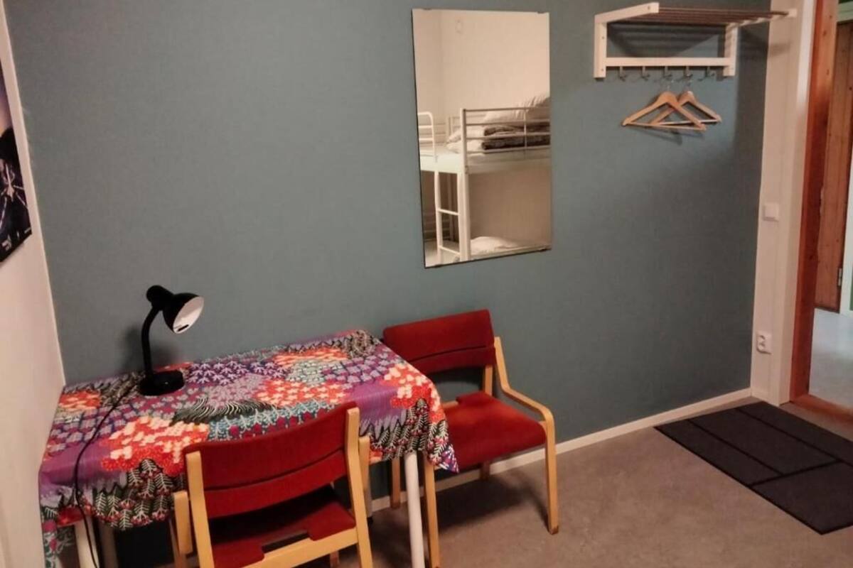 A small room with a single table and chair, a desk lamp, a mirror, and a coat rack.
