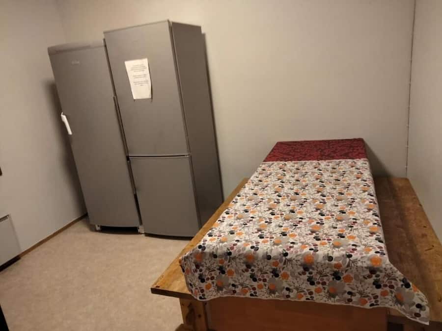 A small room with a bed, a wooden bench, and a refrigerator.