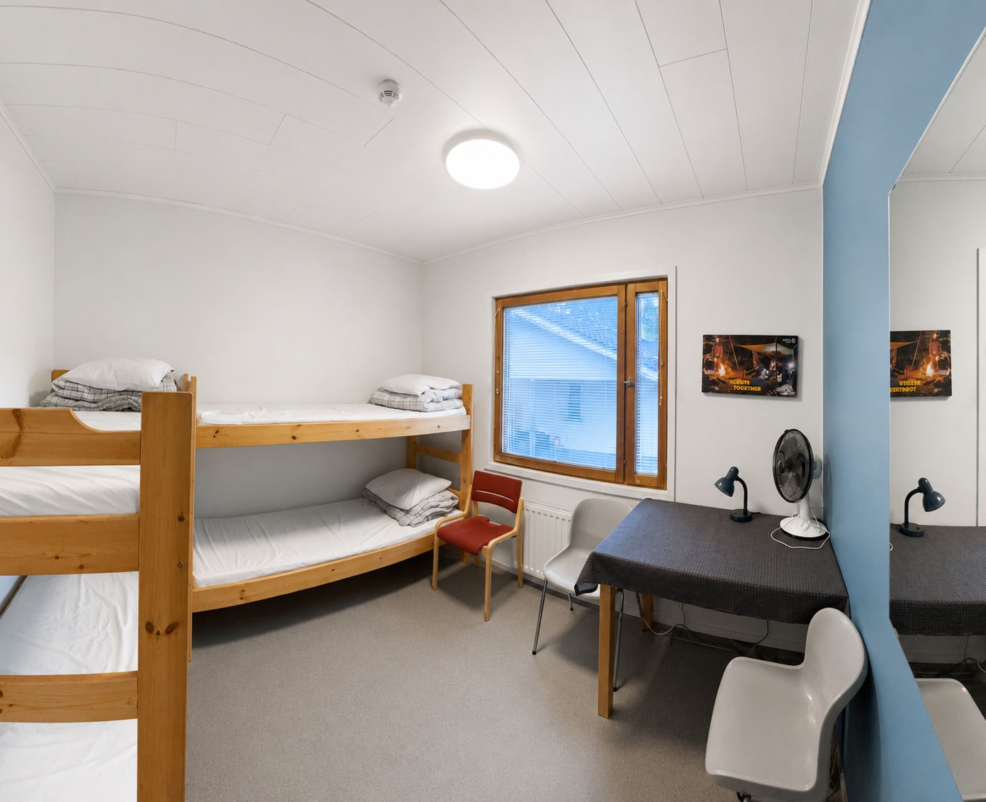 Une chambre de dortoir équipée de lits superposés, d’un bureau, d’une chaise, d’un radiateur et d’une fenêtre avec des stores.