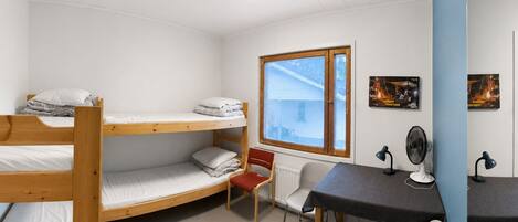 Un dormitorio con literas, un escritorio, una silla, un radiador y una ventana con persianas.