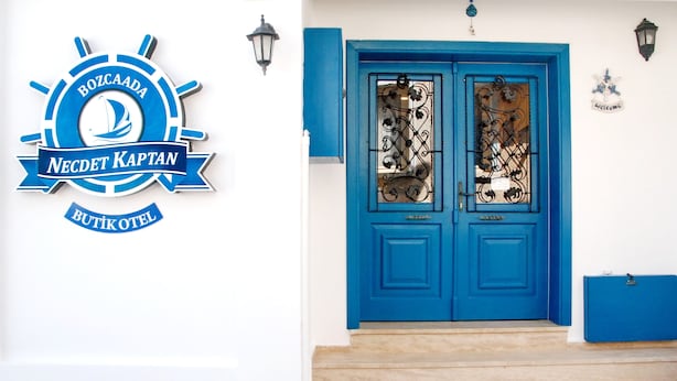 A blue door with decorative glass panels and a sign with a sailboat logo. - Necdet Kaptan Bozcaada (Bozcaada)