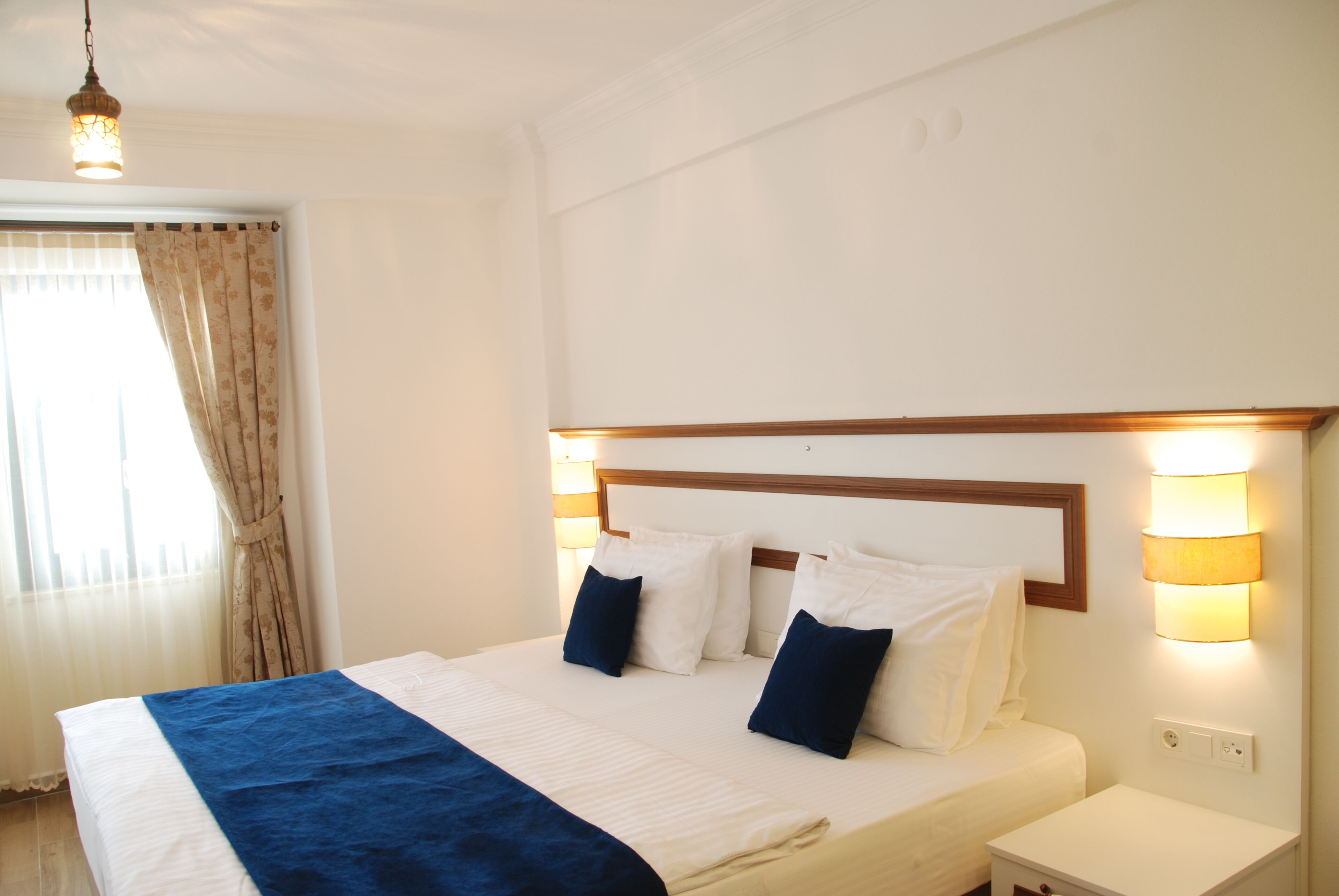 A neatly made bed with a blue blanket, white pillows, and a wooden headboard. There is a nightstand with a lamp on it.