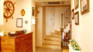 A wooden reception desk with a ship's wheel, framed certificates, and a staircase leading to a second floor. - Necdet Kaptan Bozcaada (Bozcaada)