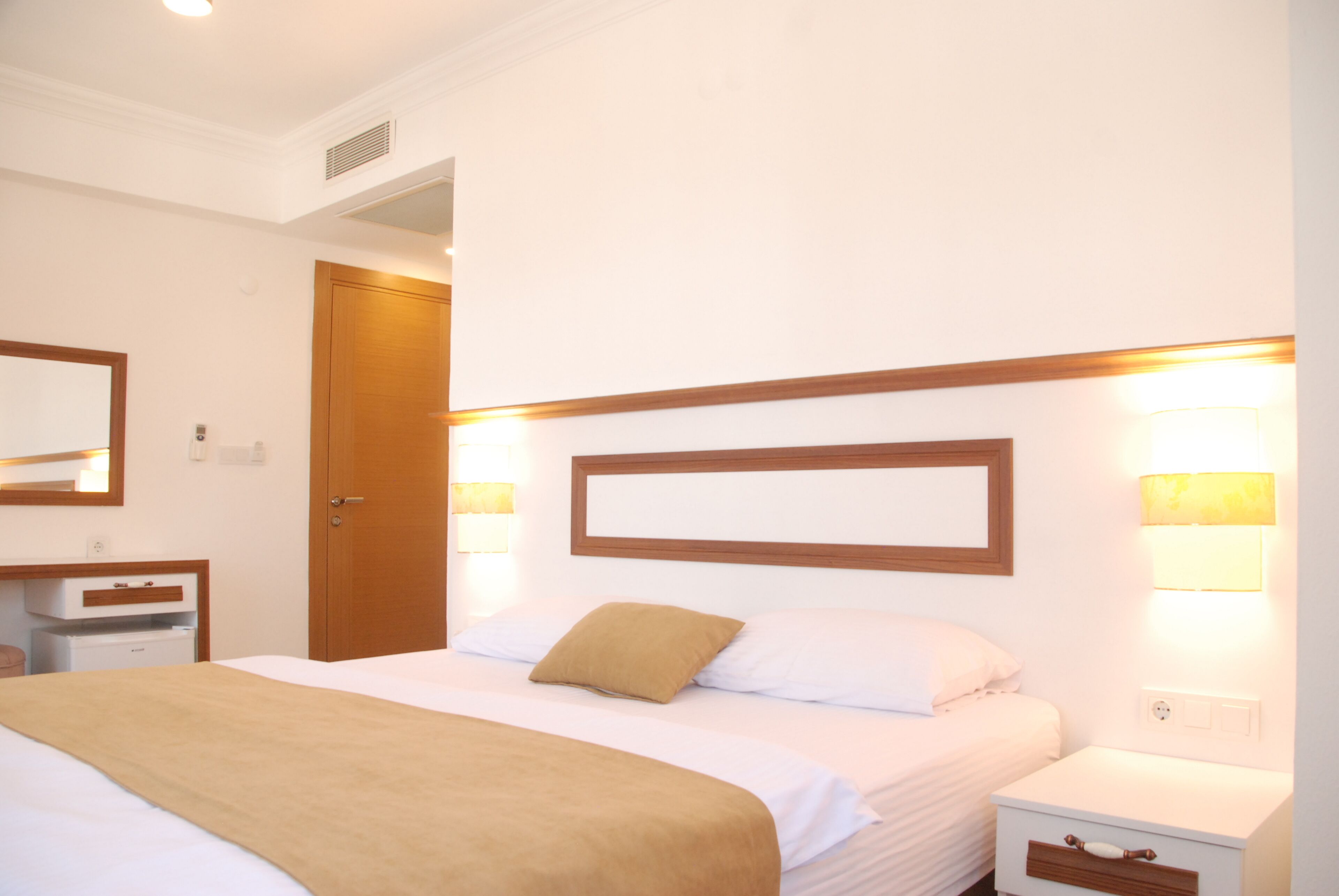 Una habitación de hotel con cama, mesita de noche, lámpara y puerta de madera.