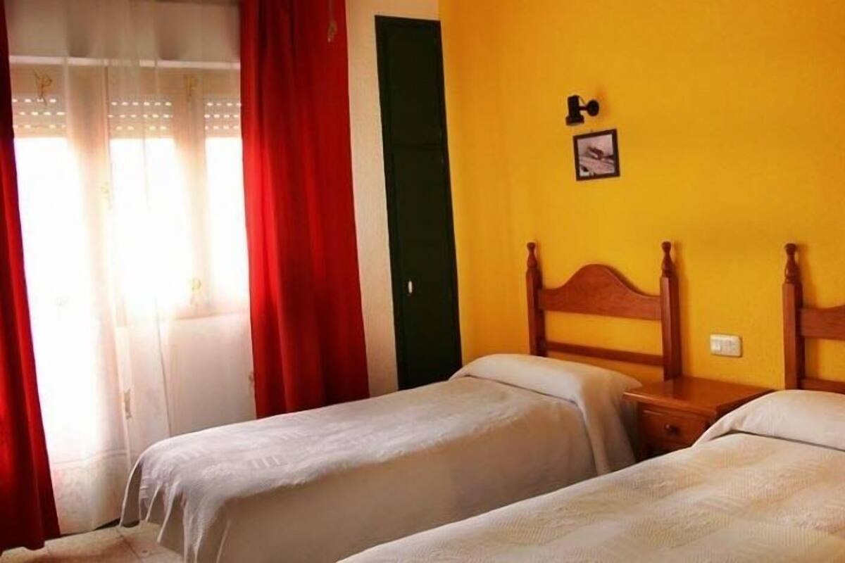 Ein Zimmer mit zwei Einzelbetten, einem hölzernen Kopfteil, einer grünen Tür und einer gelben Wand mit zwei kleinen Bildern.