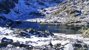 Un paisaje montañoso con un lago rodeado de rocas nevadas y terreno accidentado.